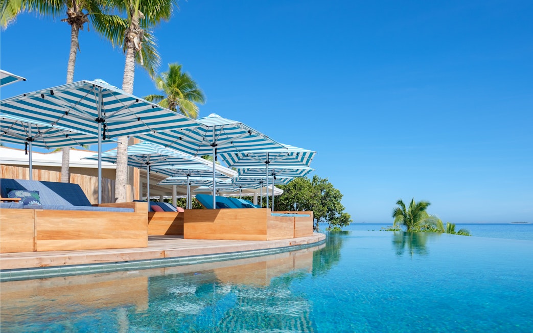 Infinity pool with striped umbrellas at Malamala Beach Club, Fiji, overlooking the ocean.