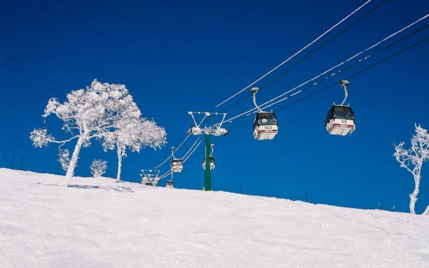 Ski lift ascending snowy slope at Rusutsu, Japan, with clear blue sky.