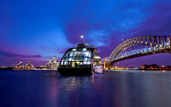 Glass boat on Sydney Harbour with views of the Opera House and Harbour Bridge at dusk.