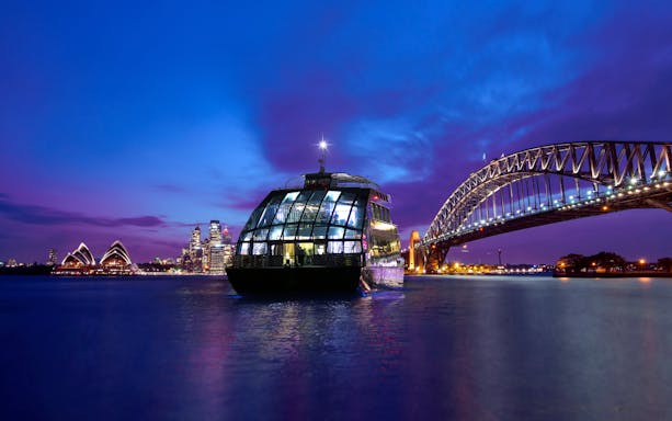 Glass boat on Sydney Harbour with views of the Opera House and Harbour Bridge at dusk.