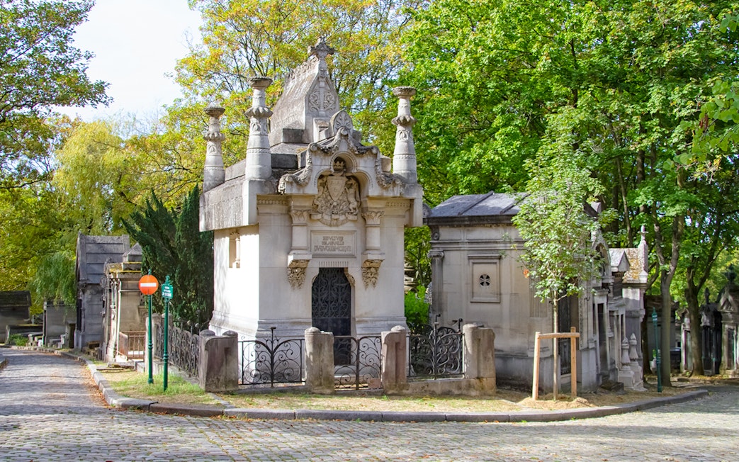 Père Lachaise Cemetery mausoleum surrounded by trees and cobblestone path.