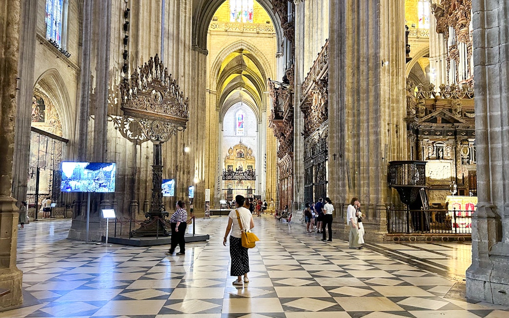Interior of Seville Cathedral with visitors exploring the ornate architecture and high vaulted ceilings.