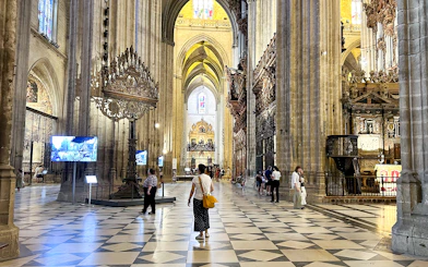 Interior of Seville Cathedral with visitors exploring the ornate architecture and high vaulted ceilings.