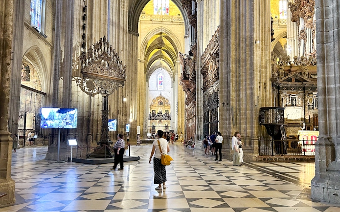 Interior of Seville Cathedral with visitors exploring the ornate architecture and high vaulted ceilings.