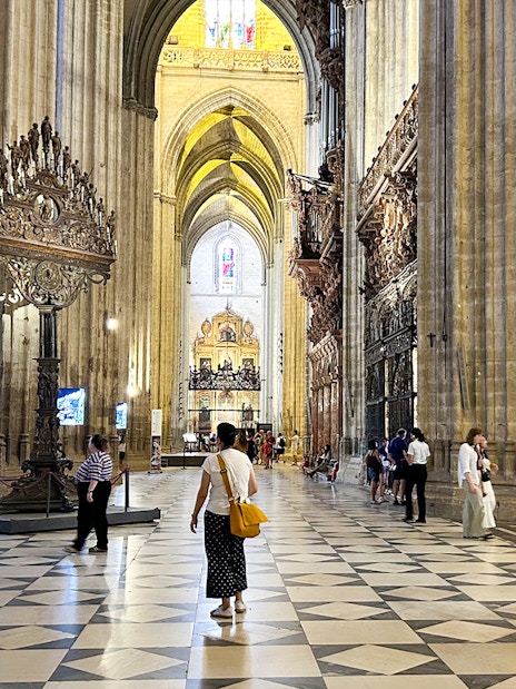 Interior of Seville Cathedral with visitors exploring the ornate architecture and high vaulted ceilings.