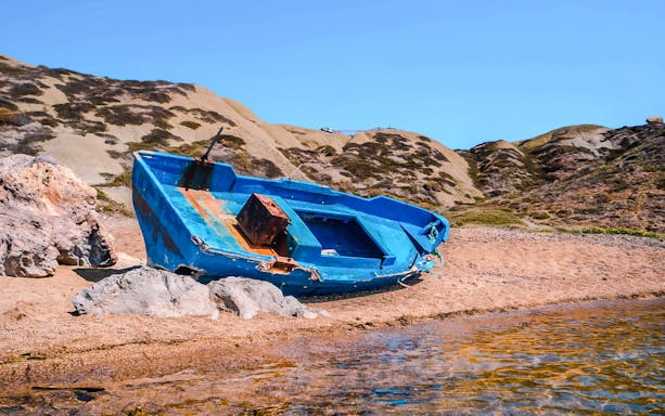 Abandoned blue boat on sandy shore near Scala Dei Turchi cliffs.