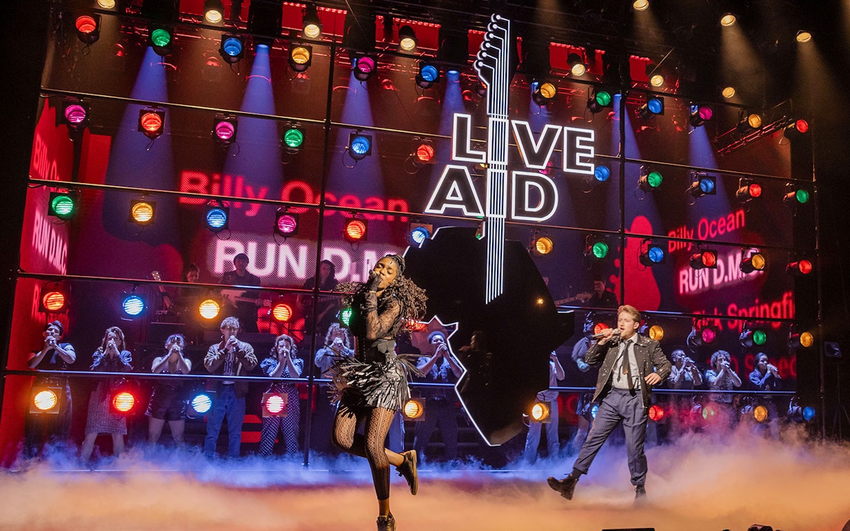 Live Aid performance at Just for One Day with singers and vibrant stage lights.