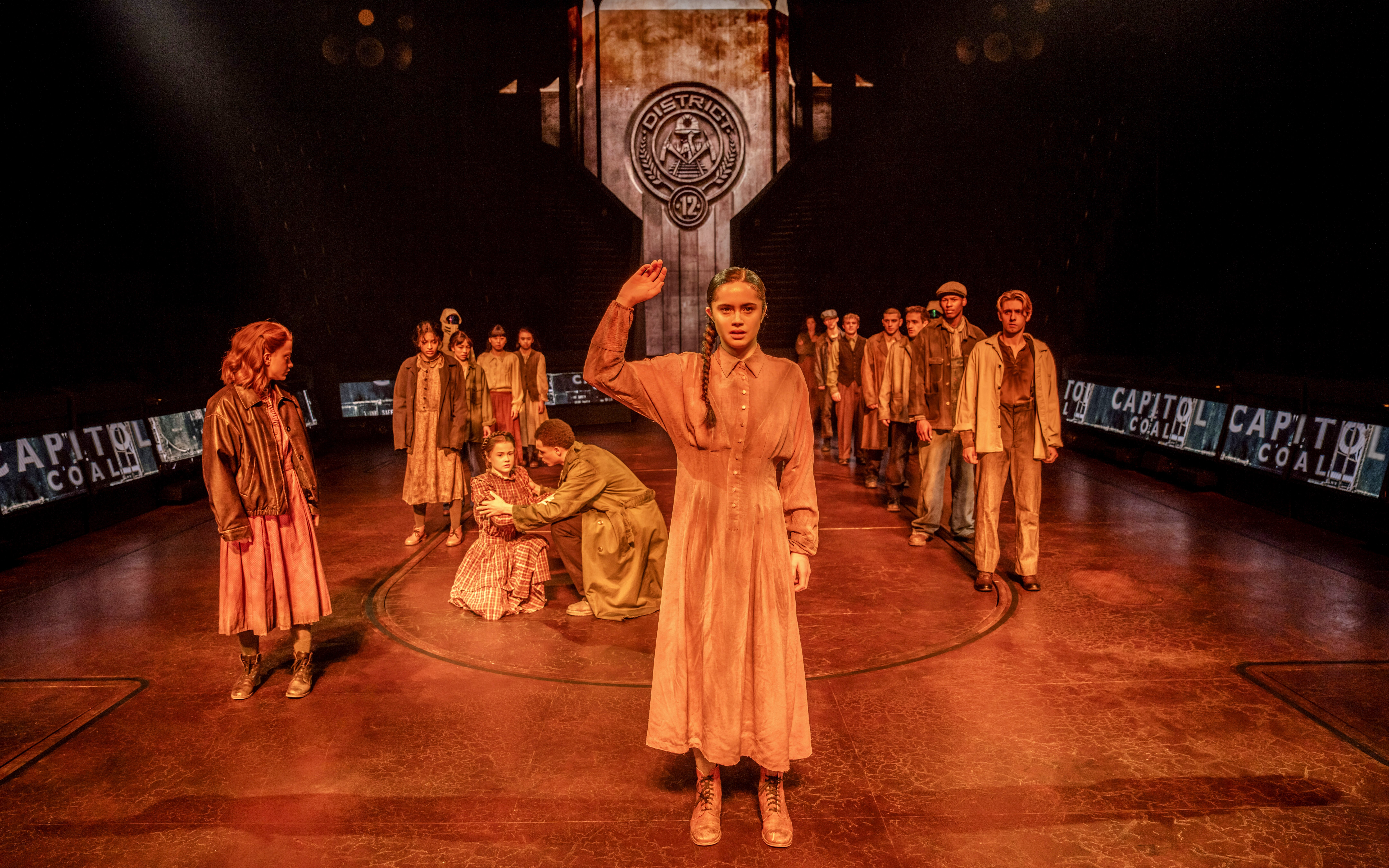 Stage scene from Hunger Games West End show with actors in District 12 setting.