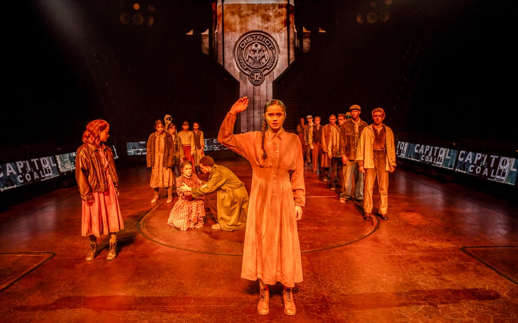 Stage scene from Hunger Games West End show with actors in District 12 setting.