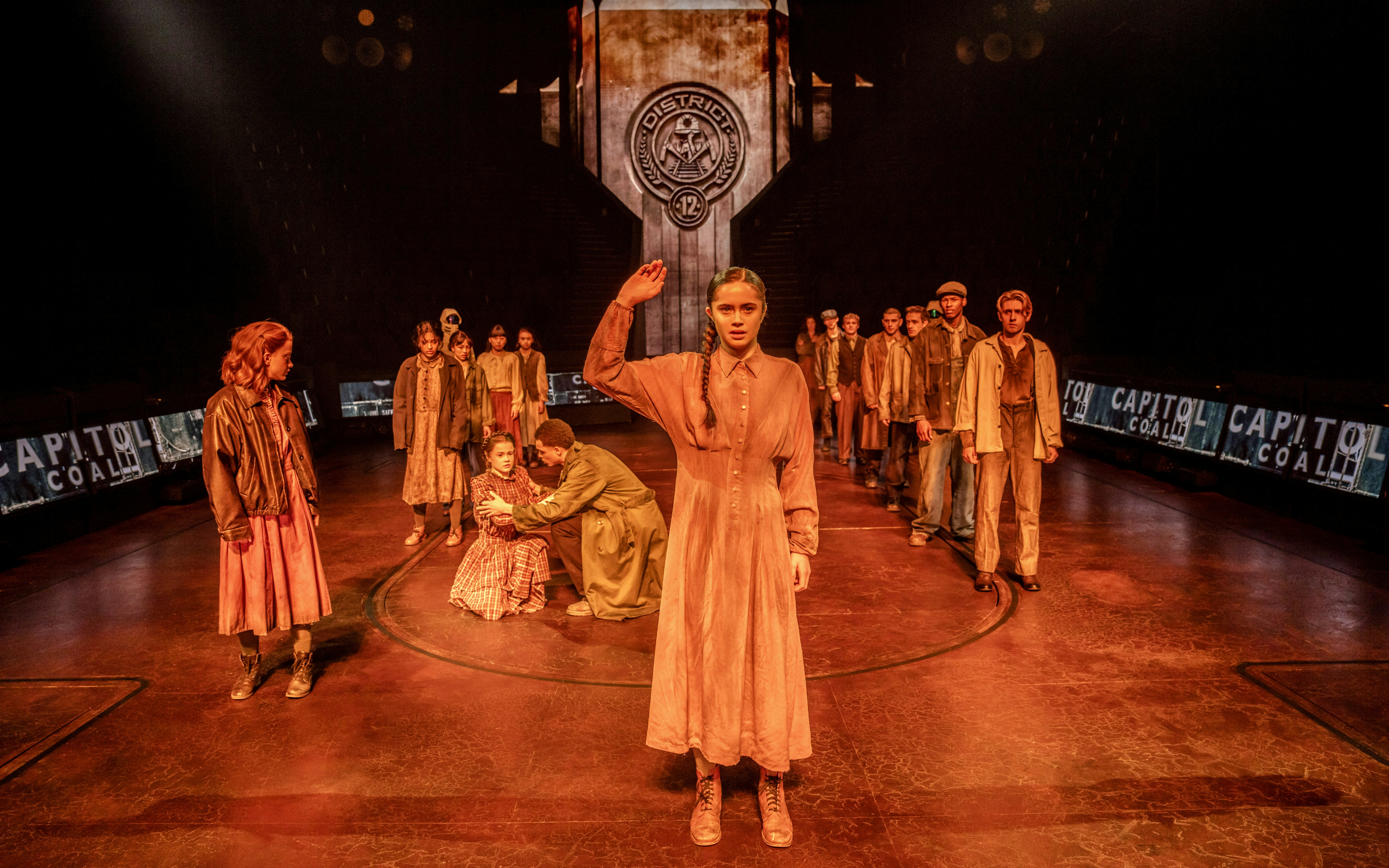 Stage scene from Hunger Games West End show with actors in District 12 setting.
