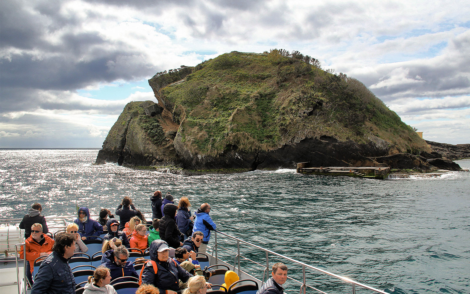 Tourists on a boat near a rocky island during a whale and dolphin watching tour.