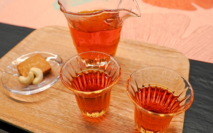 Amber-colored tea in traditional Japanese glasses on a wooden tray with snacks.