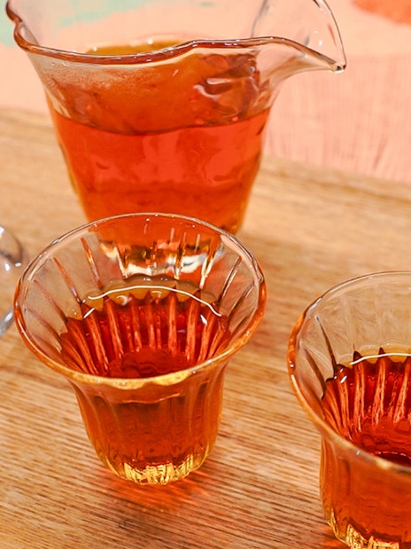 Amber-colored tea in traditional Japanese glasses on a wooden tray with snacks.