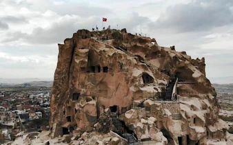 Ancient rock formations with stairs and Turkish flag in Cappadocia, part of the Red Tour.