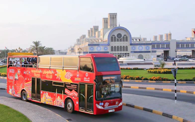 Red double-decker bus on Sharjah Hop-On-Hop-Off Tour passing Blue Souk.