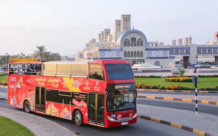 Red double-decker bus on Sharjah Hop-On-Hop-Off Tour passing Blue Souk.
