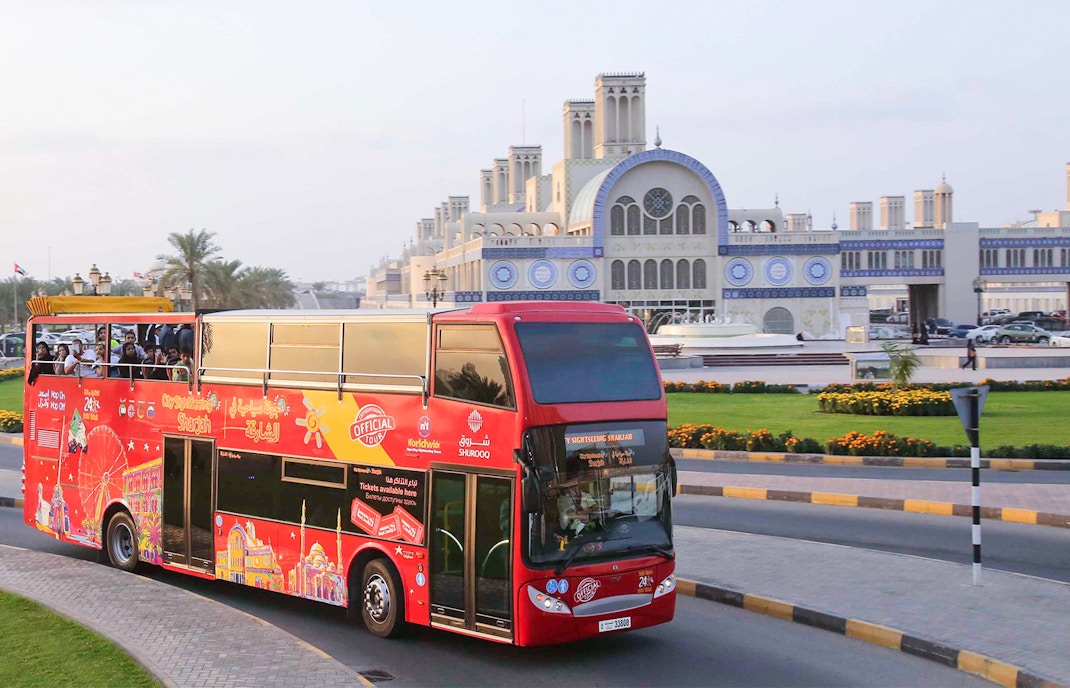 Red double-decker bus on Sharjah Hop-On-Hop-Off Tour passing Blue Souk.