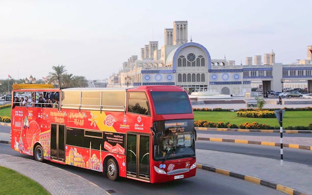 Red double-decker bus on Sharjah Hop-On-Hop-Off Tour passing Blue Souk.