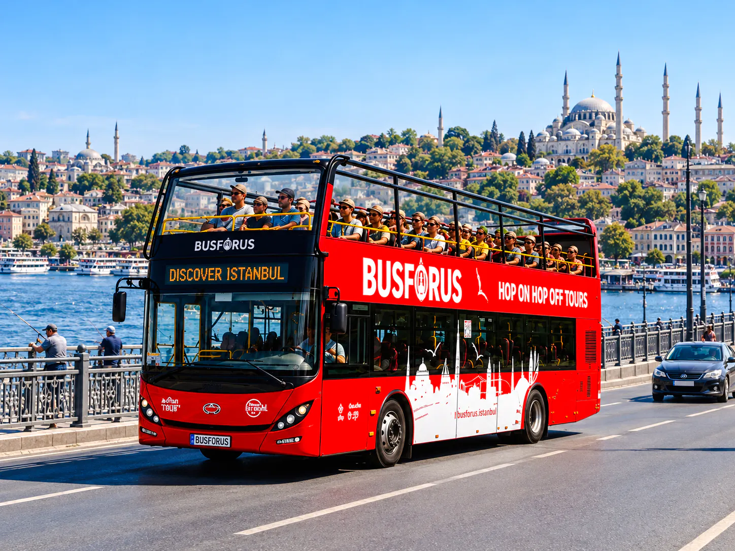 Open-top tour bus crossing a bridge in Istanbul with cityscape and mosque in the background.