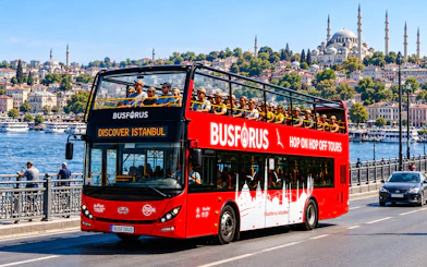 Open-top tour bus crossing a bridge in Istanbul with cityscape and mosque in the background.