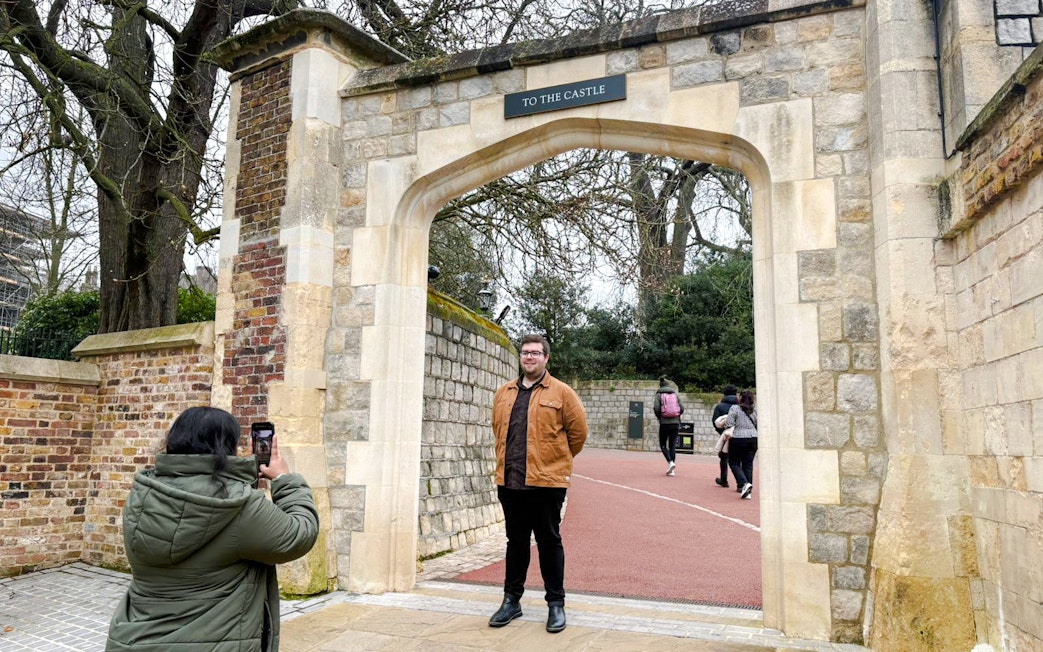 Visitors at Windsor Castle entrance, one taking a photo, others walking through the archway.