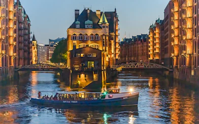 Evening cruise boat on illuminated canal in Hamburg's Speicherstadt district.