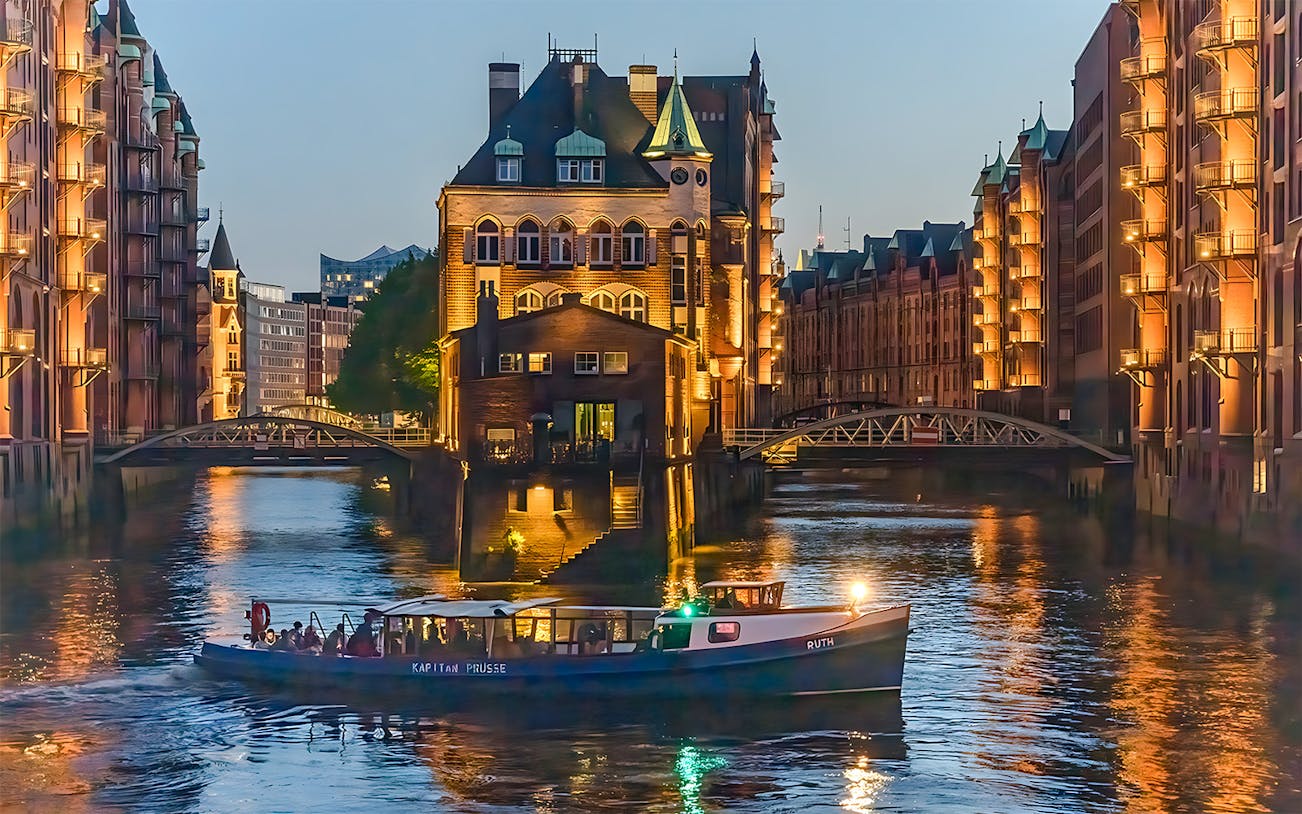 Evening cruise boat on illuminated canal in Hamburg's Speicherstadt district.
