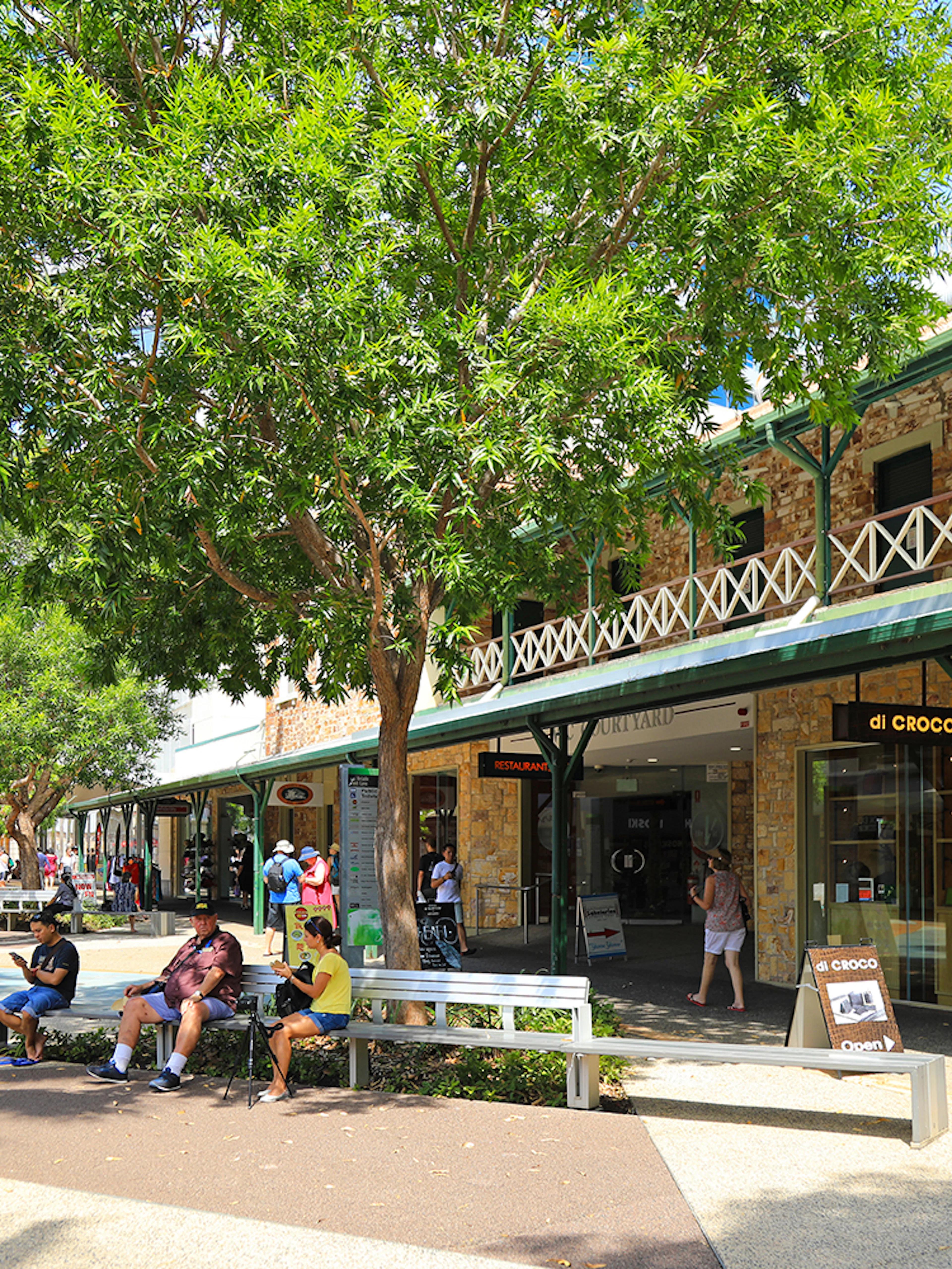 Outdoor shopping area in Darwin with people sitting and walking, part of a guided half-day city tour.