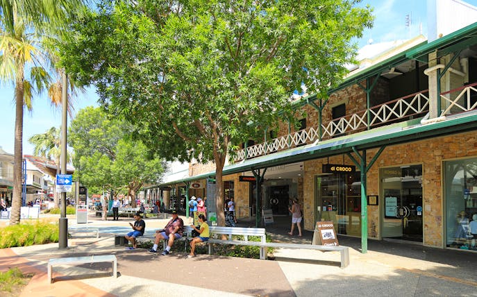 Outdoor shopping area in Darwin with people sitting and walking, part of a guided half-day city tour.