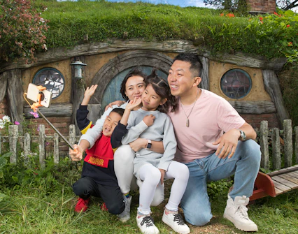 Family taking a selfie in front of a hobbit house at Hobbiton Movie Set, New Zealand.