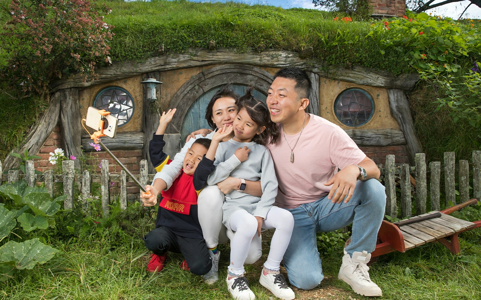 Family taking a selfie in front of a hobbit house at Hobbiton Movie Set, New Zealand.