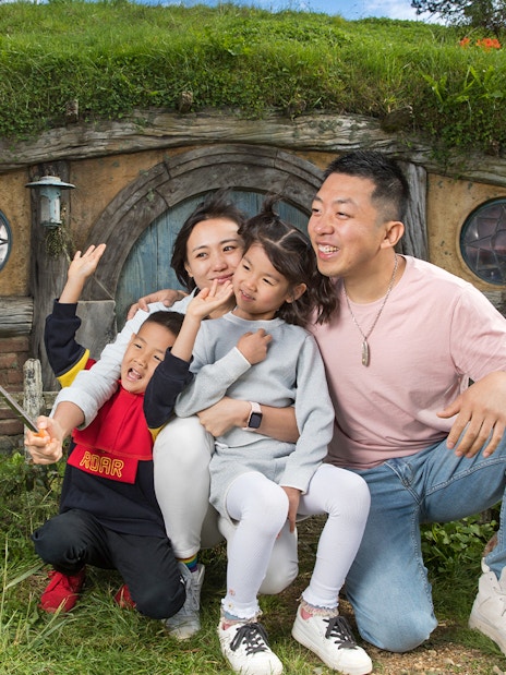 Family taking a selfie in front of a hobbit house at Hobbiton Movie Set, New Zealand.