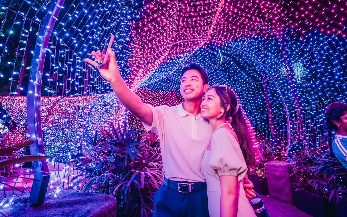 Couple taking a selfie under colorful Christmas lights at Gardens by the Bay.