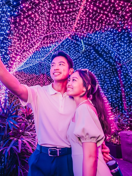 Couple taking a selfie under colorful Christmas lights at Gardens by the Bay.