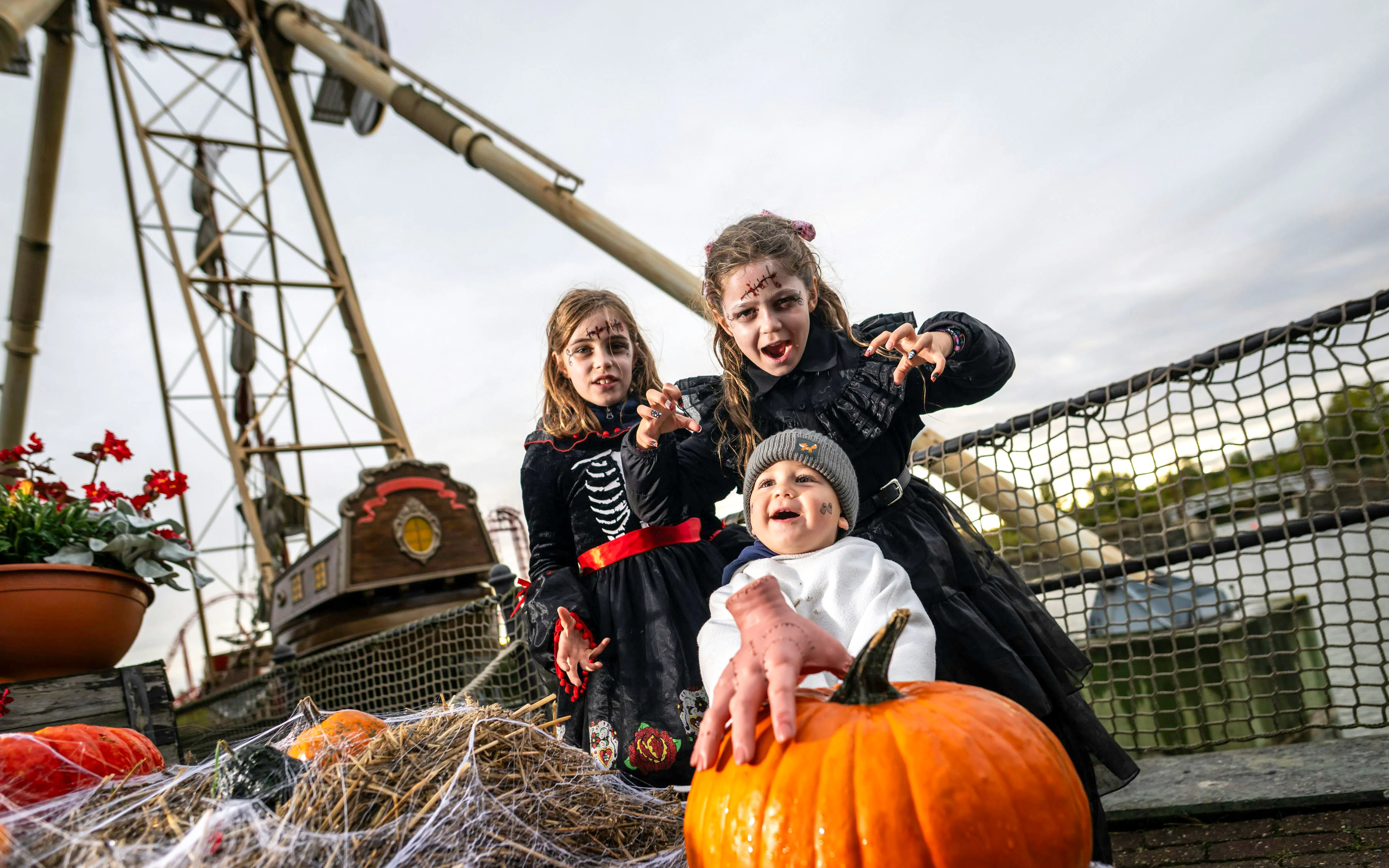 Children in Halloween costumes at Belantis Adventure Park with pumpkins and a pirate ship ride in the background.