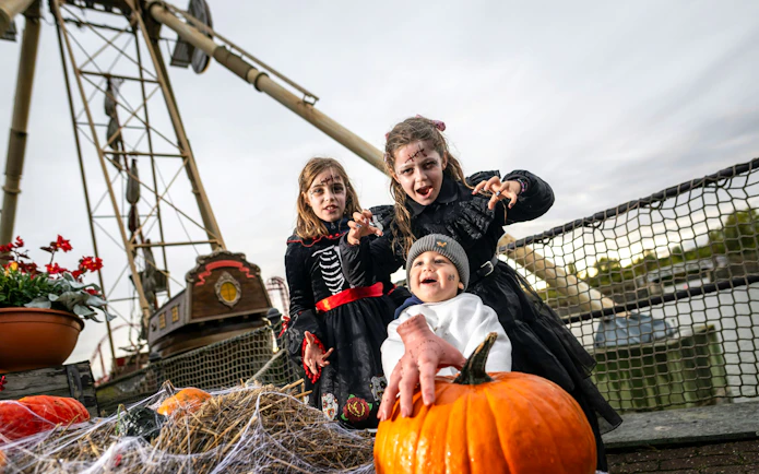 Children in Halloween costumes at Belantis Adventure Park with pumpkins and a pirate ship ride in the background.