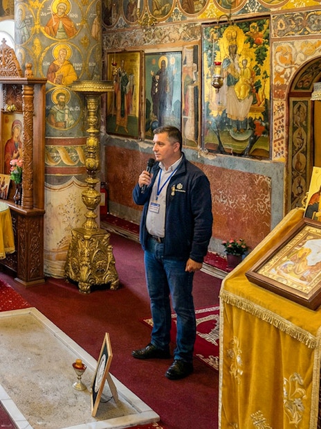 Tour guide explaining Dracula's Tomb inside Snagov Monastery to a group of visitors.