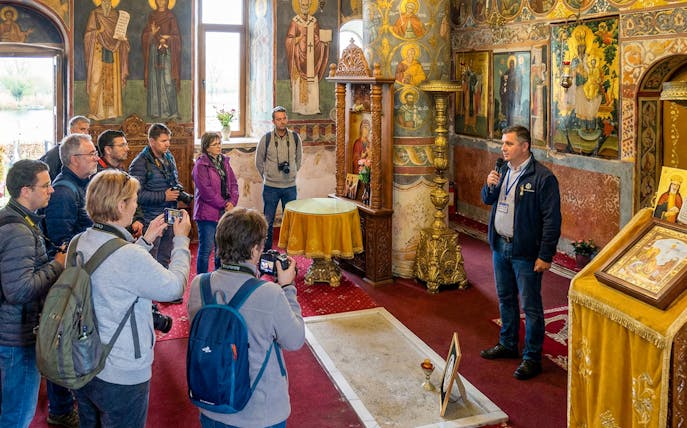 Tour guide explaining Dracula's Tomb inside Snagov Monastery to a group of visitors.
