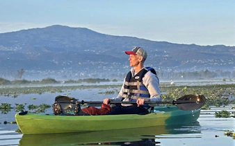 Kayaker on Xochimilco canal with mountain backdrop, guided tour.