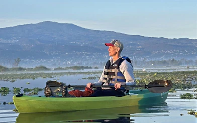 Kayaker on Xochimilco canal with mountain backdrop, guided tour.