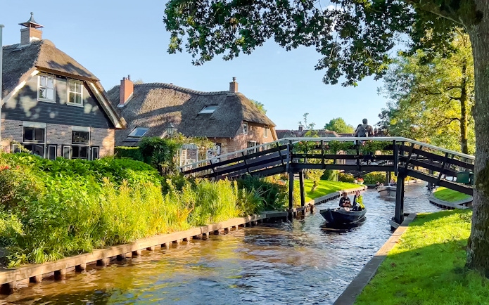 Traditional Dutch houses, gardens, and wooden bridge over canal in Giethoorn, Netherlands.