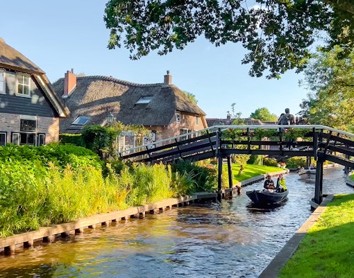 Traditional Dutch houses, gardens, and wooden bridge over canal in Giethoorn, Netherlands.