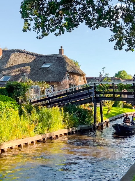 Traditional Dutch houses, gardens, and wooden bridge over canal in Giethoorn, Netherlands.