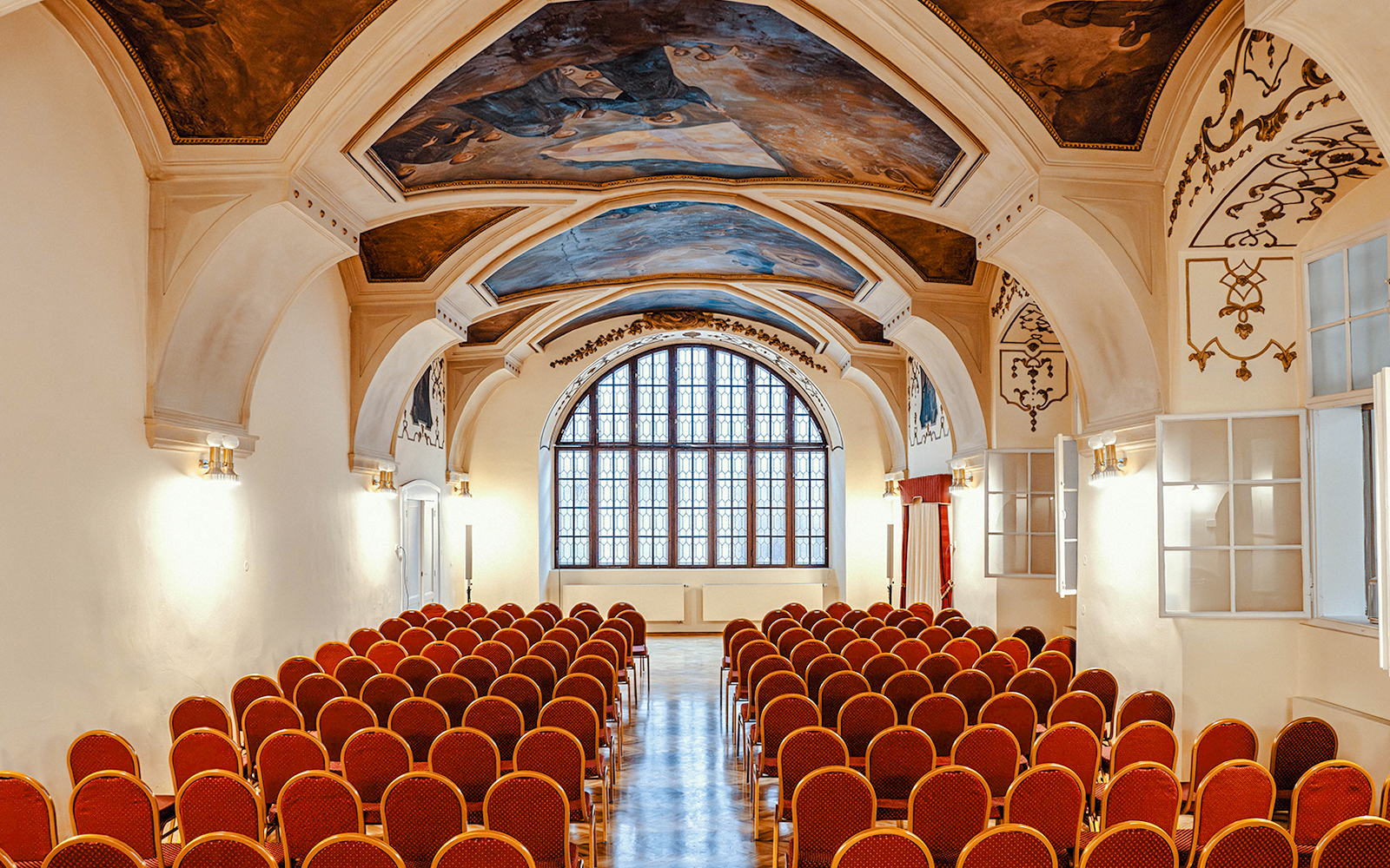Seating area inside Minorite Monastery of St James, Prague, with ornate ceiling and large window.