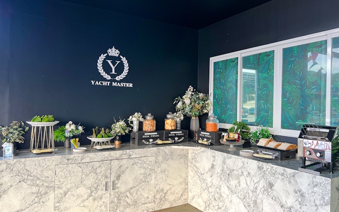 Buffet spread with snacks and drinks on marble counter, "Yacht Master" logo in background.