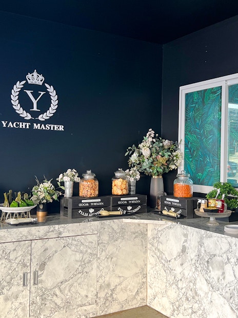 Buffet spread with snacks and drinks on marble counter, "Yacht Master" logo in background.