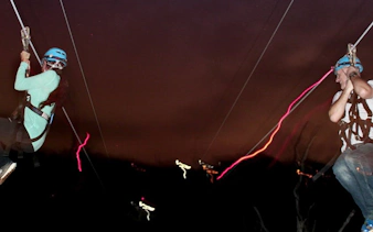 Nighttime ziplining adventure with two people under a starry sky.