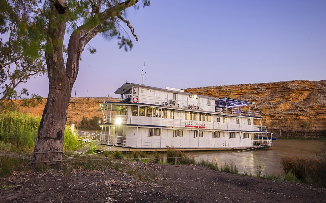 Paddle steamer on Murray River at sunset with cliffs in the background.