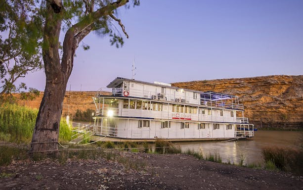Paddle steamer on Murray River at sunset with cliffs in the background.