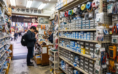 Electronics shop interior in Osaka's Den Den Town with shelves of components and customers browsing.